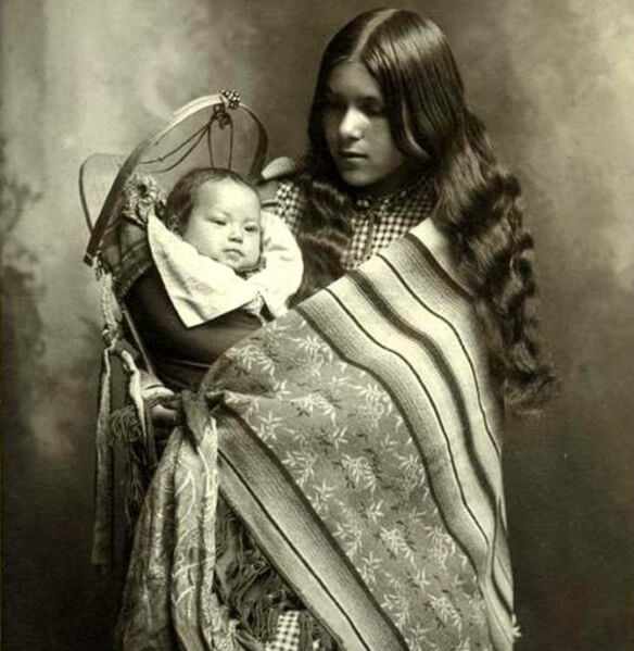A girl wearing American Indian Blankets and holding a baby